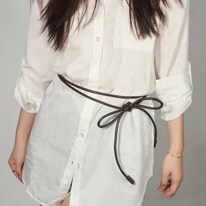 Detail of slim dark brown faux leather waist rope tied in a bow over a white shirt