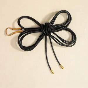 Détail d'une ceinture noire nouée avec boucle fer à cheval dorée et embouts en métal