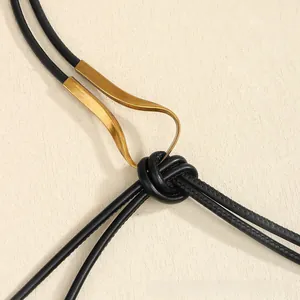 Détail d'une ceinture en corde de cuir noir avec une boucle dorée ondulée et un nœud