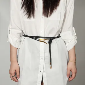 Détail d'une fine ceinture noire avec boucle dorée en fer à cheval nouée sur une robe