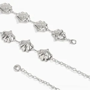 Détail d'une chaîne de taille argentée avec pendentifs en forme de coquillage et fermoir