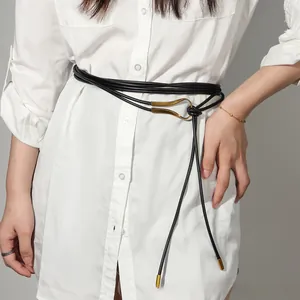 Détail d'une ceinture fine noire avec boucle crochet dorée vintage sur une chemise blanche