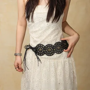 Detail of bohemian black studded leather belt with fringes on a white lace dress