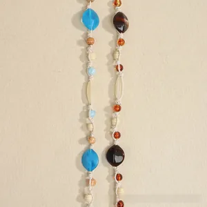 Detail of bohemian woven waist rope featuring amber and blue beads on beige cord