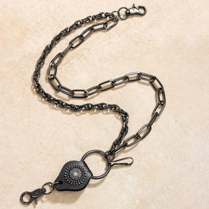 Detail of vintage punk pants chain with lobster clasps and black sunburst leather charm