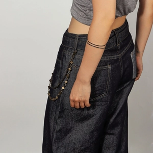 Détail de chaînes métalliques vintage avec carrés sur un jean bleu foncé à jambes larges