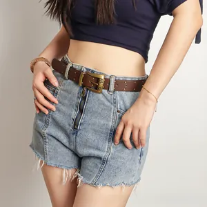 Détail d'une ceinture vintage en cuir marron avec boucle en laiton sur short en jean