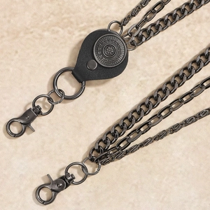 Detail of multi-layer gunmetal chains with sunburst leather patch and spring snap hooks