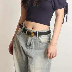 Détail de ceinture vintage noire en PU avec boucle dorée gravée sur un jean bleu clair
