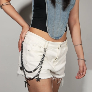 Détail d'une chaîne de taille punk en métal avec pendentifs étoiles noires sur short en jean
