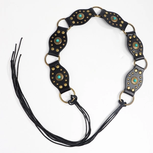 Détail d'une ceinture bohème noire avec clous turquoise, anneaux dorés et longs glands
