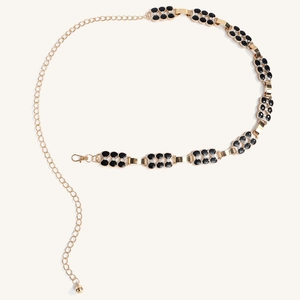Détail de la chaîne de taille dorée avec trèfles noirs et strass brillants sur fond blanc