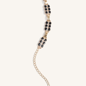 Détail d'une chaîne en métal doré vintage avec trèfles noirs et petits strass