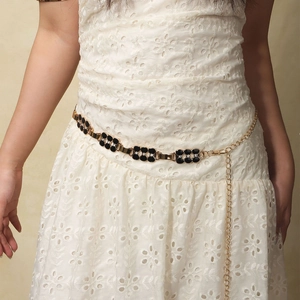 Détail d'une chaîne de taille dorée avec trèfle noir sur une robe en dentelle