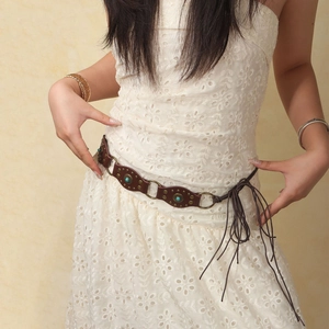 Détail d'une ceinture bohème avec clous turquoise, anneaux en métal et franges en cuir