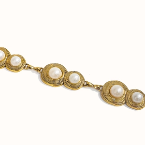 Macro detail of vintage gold chain belt featuring pearl-inlay spiral textured links