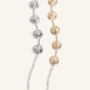 Dettaglio di catene da vita in metallo argento e oro con texture a raggi di sole e maglie
