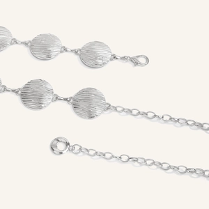 Dettaglio cintura a catena argento con chiusura a moschettone e dischi con texture a onde