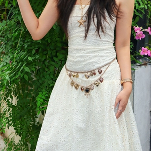 Detail of multilayer gold heart chain belt on white lace dress in a garden setting