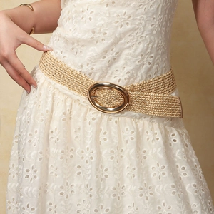 Detalle de cinturón trenzado beige con hebilla ovalada dorada en vestido de encaje