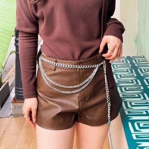 Detail eines silbernen mehrlagigen Metallketten-Gürtels kombiniert mit braunen Shorts