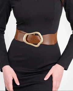 Detail of a brown wide elastic waist belt with a gold asymmetrical buckle on a black dress