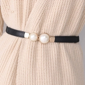 Close-up of elegant gold buckle with double pearls on a slim black elastic belt for women