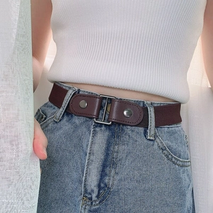 Detail of coffee brown elastic belt with silver metal buckle and brown leather ends on jeans