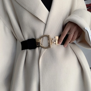 Detail of black elastic waist belt with large gold OT buckle on a beige coat