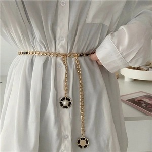 Détail d'une ceinture chaîne dorée avec pendentifs fleurs noires sur robe plissée blanche