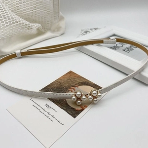 Detail van een dunne witte lederen riem met een gouden gesp bezet met witte parels