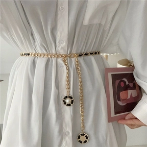 Détail de la ceinture chaîne dorée entrelacée de cuir noir et breloques camélia