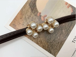 Gros plan sur la boucle trèfle en perles d'une fine ceinture en cuir marron