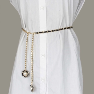 Détail de la chaîne de taille dorée avec sangle tissée noire et breloques de fleurs