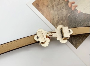 Détail de la boucle trèfle dorée sur une ceinture fine en cuir kaki pour robes