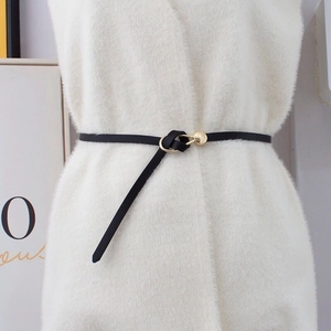 Close-up of black leather slim belt with gold round buckle on white knit sweater