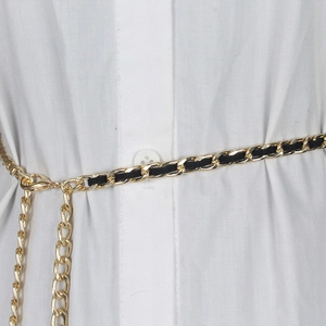 Détail de la chaîne en métal doré et ceinture en cuir noir sur une chemise blanche