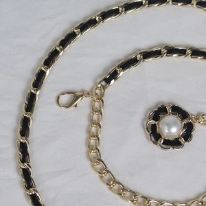 Détail de la ceinture chaîne en métal doré avec tissage en cuir noir et perle fleur