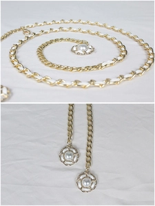 Détail d'une chaîne dorée entrelacée de cuir blanc avec des pendentifs floraux en perles