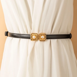 Close-up of thin black leather belt with gold buckle and pearl detail on white dress