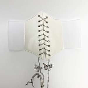Détail d'un corset blanc avec chaînes croisées argentées et breloques papillon