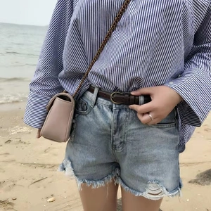 Close-up of vintage brown leather belt styled with distressed blue denim shorts and fringe