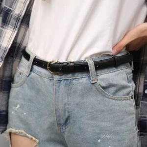 Close-up of a slim black vintage leather belt with a bronze buckle on denim shorts