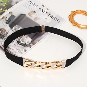 Detail of black elastic belt with chunky gold chain buckle on magazine background