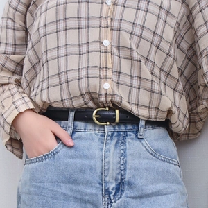 Close-up of a slim black leather belt with golden D-ring buckle on light blue jeans