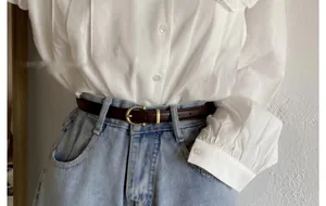 Détail d'une fine ceinture en cuir marron foncé avec boucle dorée sur un jean bleu