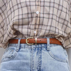 Ceinture fine en cuir marron avec boucle fer à cheval dorée portée sur un jean bleu