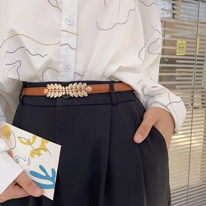 Elegant thin brown leather belt for women featuring a golden leaf-shaped buckle on trousers
