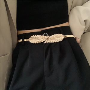 Detail of a golden leaf buckle on a slim elastic metal belt for dresses and suits