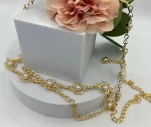 Détail de la chaîne de taille dorée avec perles blanches et motifs de fleurs